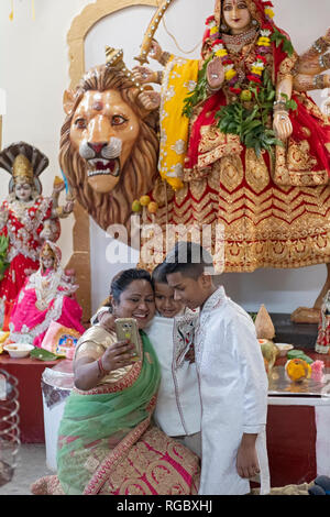 Una madre indù in un sari prende un selfie di se stessa e i suoi figli di fronte fo una statua della divinità Durga. In Giamaica, Queens, a New York City. Foto Stock