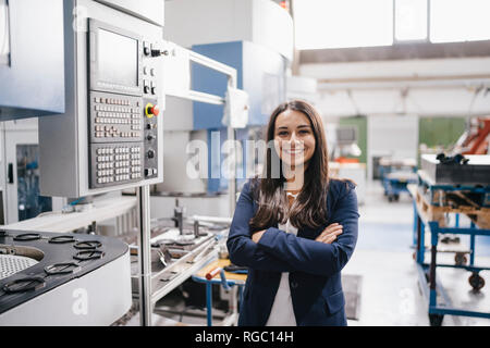 Fiducioso donna che lavorano in high tech enterprise, stando in officina in fabbrica con le braccia incrociate Foto Stock
