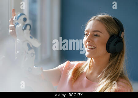 Ritratto di sorridente giovane donna con cuffie guardando robot giocattolo Foto Stock