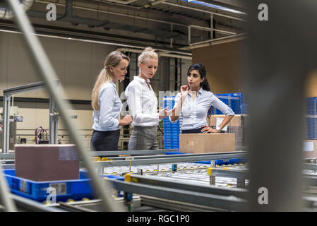 Tre donne discute al nastro trasportatore in fabbrica Foto Stock