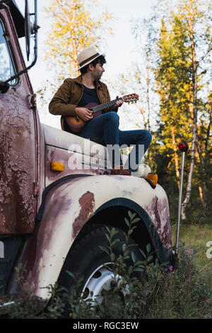 Giovani amn seduto su un carrello rotto, giocando l'ukulele Foto Stock