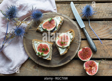 Fette di pane imburrate con spicchi di fichi sul piatto di legno Foto Stock