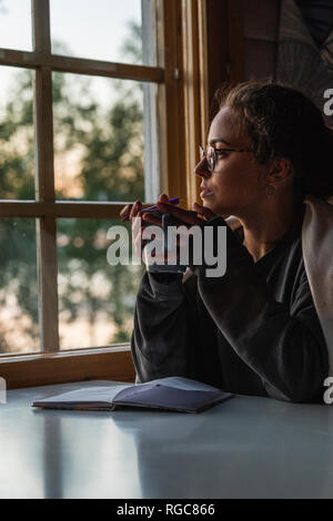 Finlandia, Lapponia, giovane donna seduta alla finestra tenendo una tazza Foto Stock