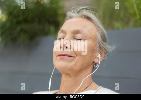 Ritratto di donna senior con gli occhi chiusi che indossa gli auricolari all'aperto Foto Stock