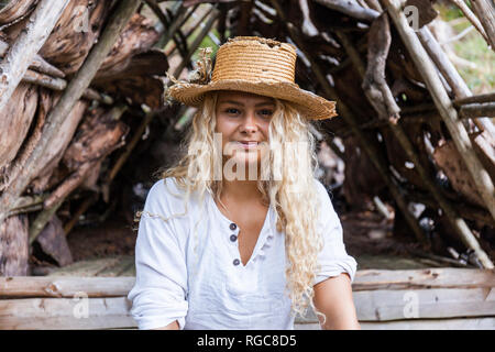 Ritratto di giovane sorridente donna che indossa cappello di paglia al rifugio in legno Foto Stock