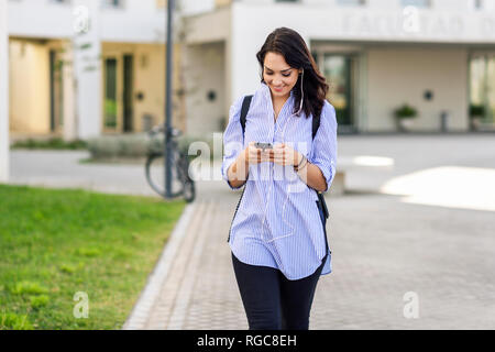 Ritratto di sorridere studente utilizza lo smartphone e gli auricolari Foto Stock