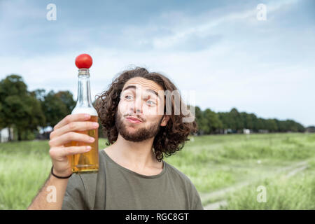 Ritratto di giovane sorridente uomo all'aperto di pomodoro di bilanciamento sulla bottiglia di birra Foto Stock