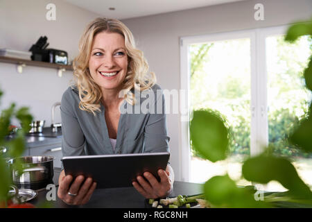 Donna sorridente con tablet in cucina Foto Stock