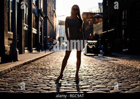 Stati Uniti d'America, New York, Brooklyn, Dumbo, silhouette della giovane donna in piedi sulla strada di retroilluminazione Foto Stock