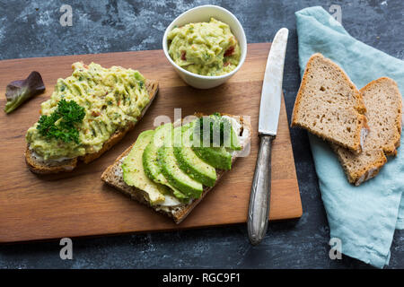 Fette di pane con fette di avocado e crema di avocado su pannello di legno Foto Stock