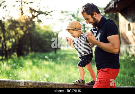 Padre assistere il suo piccolo figlio in equilibrio su una recinzione Foto Stock