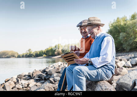 Due vecchi amici seduti in Riverside, utilizzando tavoletta digitale Foto Stock