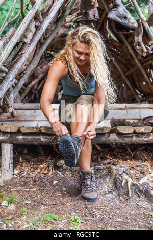 Giovane donna seduta sul banco la sua legatura scarponcini da trekking Foto Stock