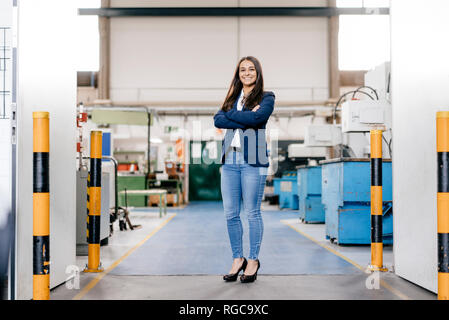 Fiducioso donna che lavorano in high tech enterprise, stando in officina in fabbrica con le braccia incrociate Foto Stock