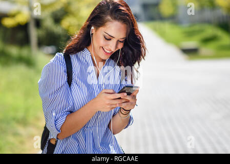 Sorridente studente utilizza lo smartphone e gli auricolari Foto Stock