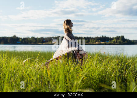 Finlandia, Lapponia, donna avvolta in una coperta in piedi sulla riva del lago Foto Stock