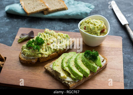 Fette di pane con fette di avocado e crema di avocado su pannello di legno Foto Stock