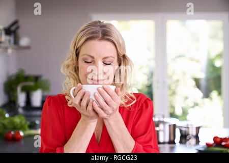 Ritratto di donna godendo di tazza di caffè in cucina Foto Stock