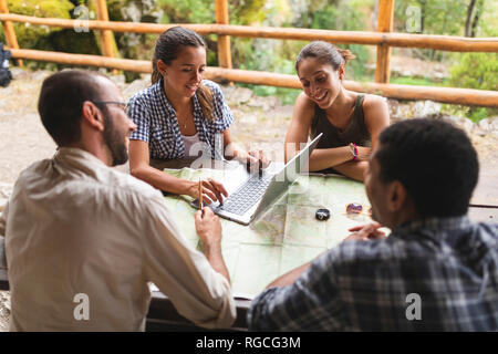 Gruppo di escursionisti seduti insieme la pianificazione di un percorso escursionistico usando la mappa e il computer portatile Foto Stock