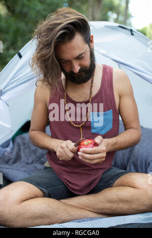 Uomo seduto di fronte ad una tenda peeling un Apple Foto Stock