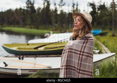 Finlandia, Lapponia, donna che indossa un cappello avvolto in una coperta permanente al lago Foto Stock