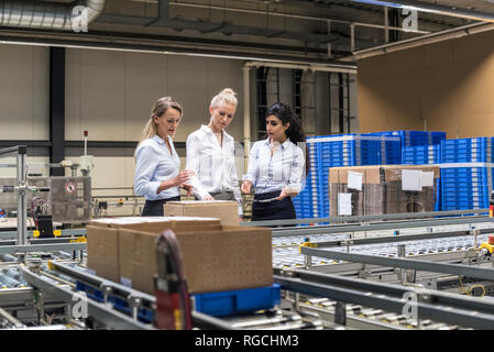 Tre donne discute al nastro trasportatore in fabbrica Foto Stock