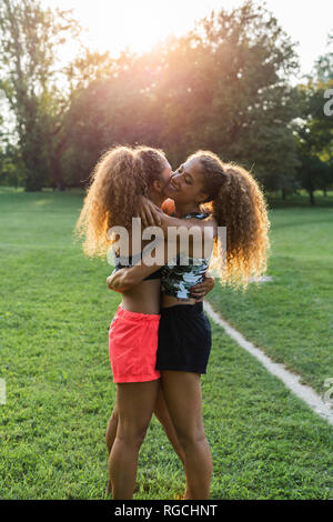 Gemelle che abbraccia ogni altra in un parco Foto Stock