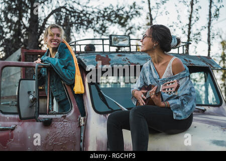 Due amici seduti su un carrello rotto, giocando l'ukulele Foto Stock