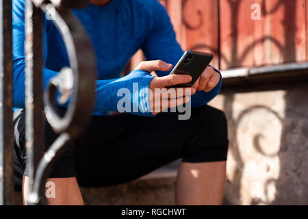 Close-up di atleta seduto sulla parte anteriore stoop tramite telefono cellulare Foto Stock