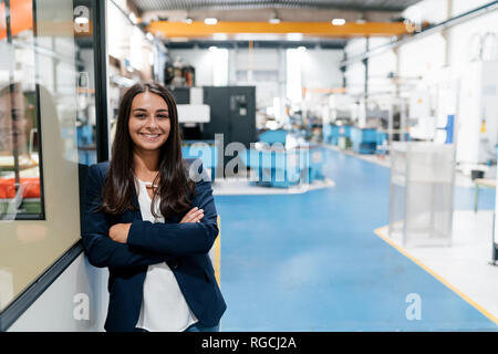 Fiducioso donna che lavorano in high tech enterprise, stando in officina in fabbrica con le braccia incrociate Foto Stock