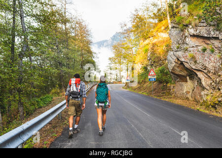 L'Italia, Massa, vista posteriore della coppia giovane camminando sulla strada asfaltata in Alpi Apuane montagne Foto Stock