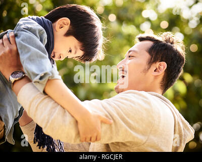 Padre asiatica divertirsi figlio di sollevamento oudoors nel parco. Foto Stock