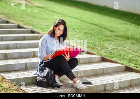 Studente seduto sulle scale all'aperto a prendere appunti in un notebook Foto Stock