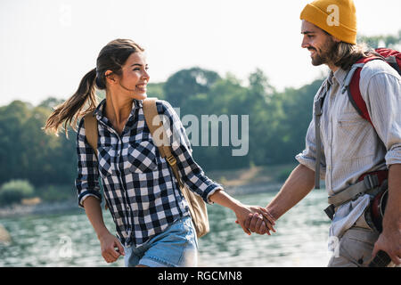 Felice coppia giovane con zaini e chitarra a piedi lungo il fiume Foto Stock