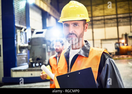 Ritratto di fiducioso uomo indossando indumenti da lavoro protettiva in fabbrica Foto Stock