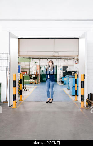 Fiducioso donna che lavorano in high tech enterprise, stando in officina in fabbrica con le braccia incrociate Foto Stock