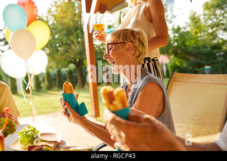 Donna felice di mangiare un hot dog su un party in giardino Foto Stock