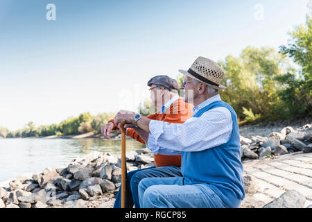 Due vecchi amici seduti su un tronco di albero, guardando il fiume Foto Stock