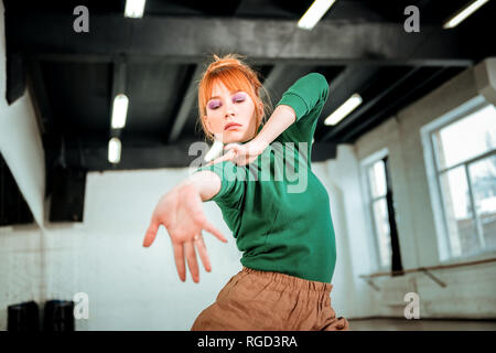 I capelli rossi professional coreografo in un verde turtleneck stretching il suo braccio Foto Stock