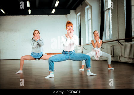 I capelli rossi insegnante di danza in jeans blu e i suoi studenti facendo squatting Foto Stock