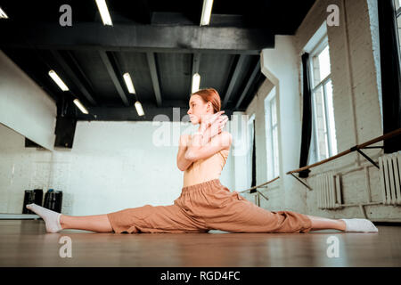 Carino i capelli rossi adolescente in arancione pantaloni facendo leg-split Foto Stock