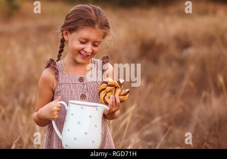 Bambina con un vasetto di latte nel counrtyside. Una delle ragazze bevande latte e mangia il pane. Foto Stock