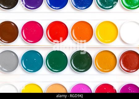 Vista superiore della tavolozza di colore bianco con vernici giacciono isolato su sfondo chiaro. Posto per iscritto. Può essere usato come un creativo dello sfondo. Brillanti colori dell'arcobaleno Foto Stock