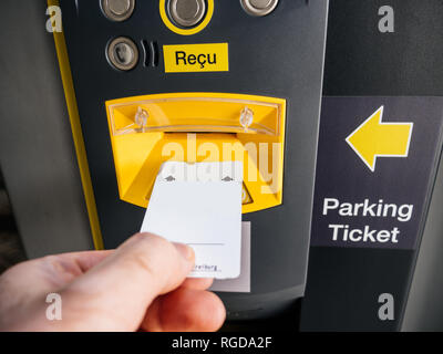 Il punto di vista della mano maschio inserendo i biglietti per il parcheggio in corrispondenza elettronica della macchina nel grande parcheggio moderno Foto Stock