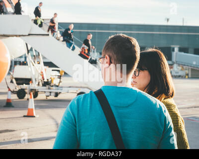 BASEL, Svizzera - Nov 11, 2018: vista posteriore di un uomo e di una donna che guarda la EasyJet Airbus piano su asfalto con passeggeri discendente dalla uscita anteriore su una luminosa giornata di sole Foto Stock