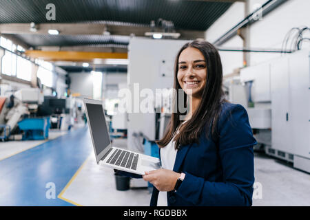 Fiducioso donna che lavorano in high tech enterprise, tenendo laptop Foto Stock