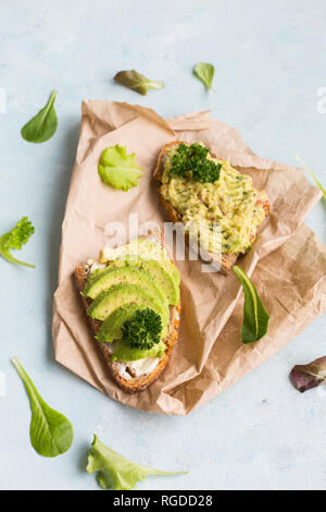 Fette di pane con fette di avocado e crema di avocado su carta marrone Foto Stock