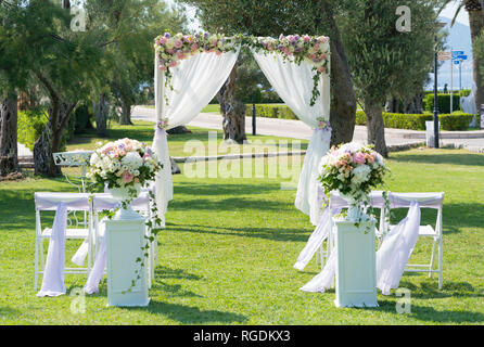 Rettangolare in legno arco di nozze e sedie decorate con fiori e tessuto per una cerimonia di nozze sul prato Foto Stock