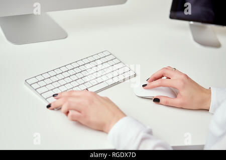 Primo piano di offuscata mani femminili digitando sulla tastiera bianca che lavora in ufficio e utilizzando i moderni computer Foto Stock