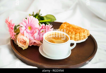 Bouquet di fiori con tazza di caffè e pasticceria bun sul vassoio in legno nel letto, mattina bed breakfast, romantico letto lo stile di vita di caffè Foto Stock